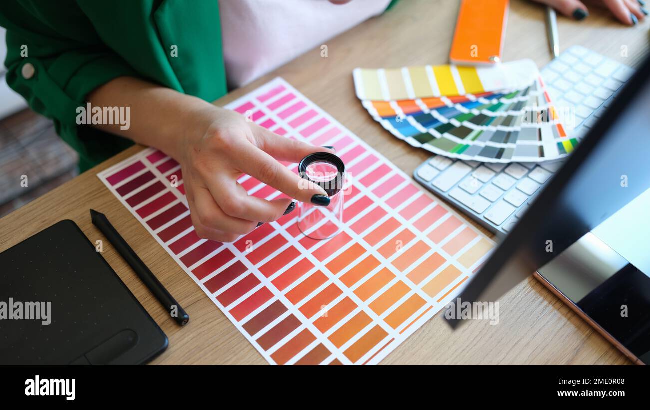 Designer con lente d'ingrandimento lavora con la scala pantone in studio d'arte. Foto Stock