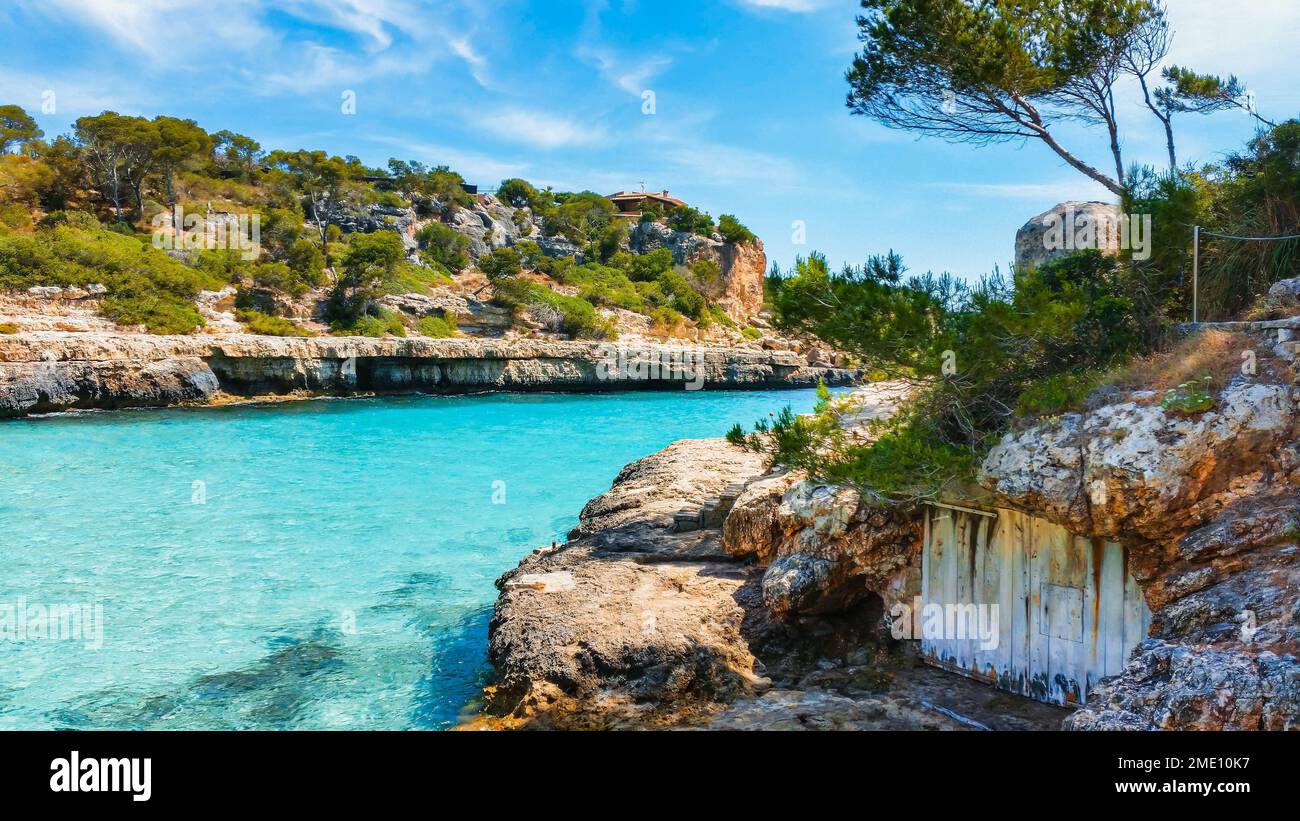 Un idilliaco paesaggio costiero con scogliere boscose e acqua blu sulla spiaggia di Llombards a Maiorca Foto Stock