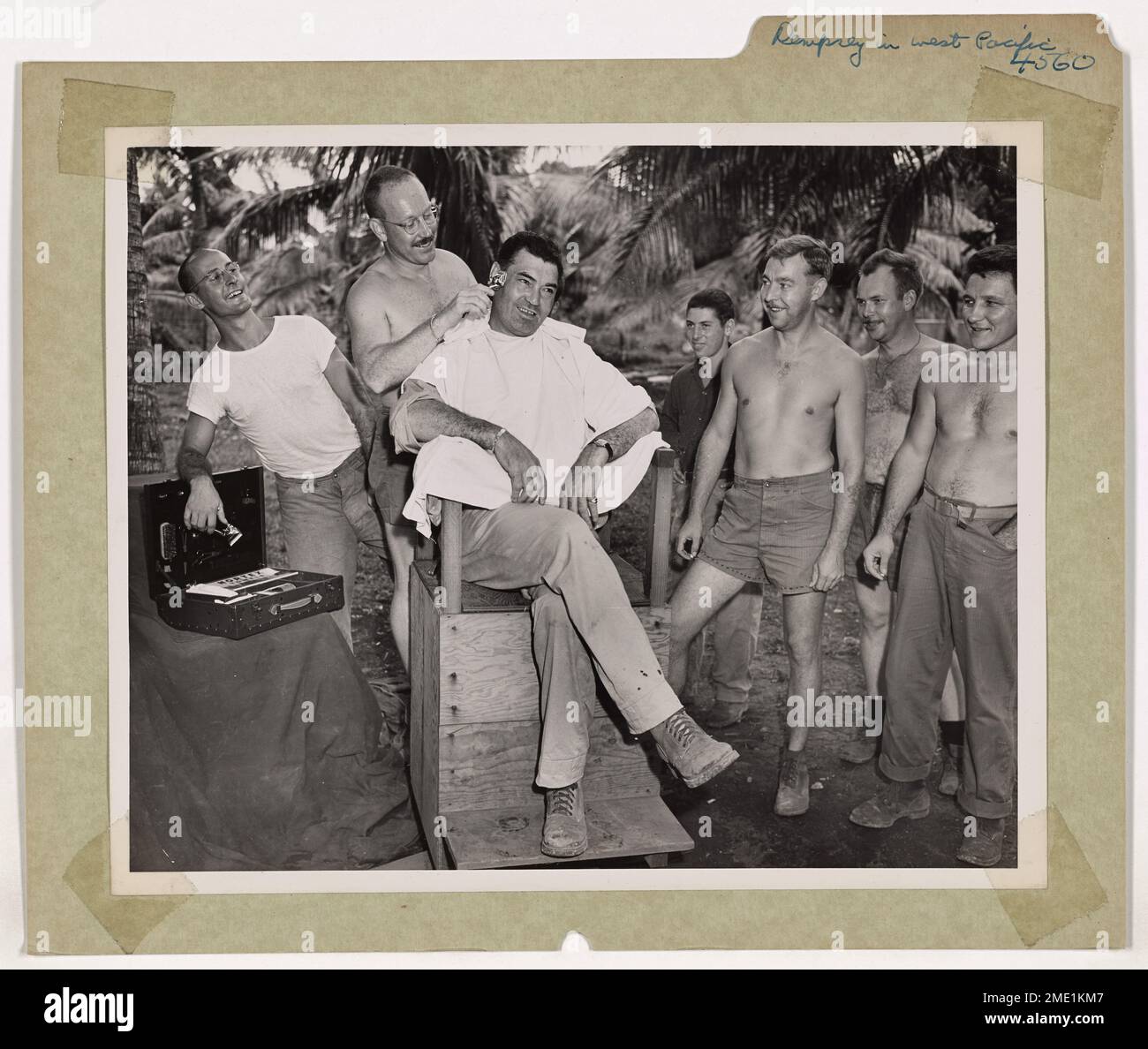 In una remota base dell'isola della Guardia Costiera nel Pacifico occidentale, l'ex campione dei pesi massimi Jack Dempsey visita un barbiere sotto le palme. Durante il suo tour in trotto del globo, Dempsey osservò personalmente come il suo programma di fitness di Manhattan Beach aveva preparato gli uomini della Guardia Costiera per il combattimento. La sua visita gli ha permesso di entrare in contatto con i membri del servizio che aveva addestrato, migliorando ulteriormente il morale e la prontezza. Foto Stock