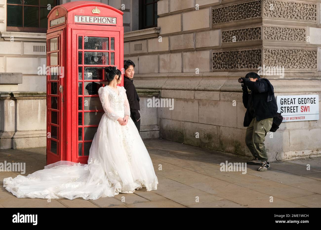 Una sposa e uno sposo posa per un fotografo di fronte a un iconico telefono rosso nel centro di Londra, gennaio, 2023 Foto: Jacquelin Magnay Foto Stock