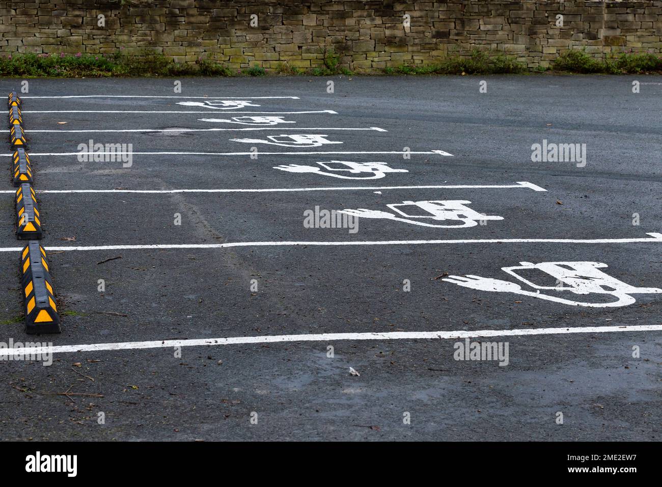 Una fila di vani auto per la ricarica di veicoli elettrici. Le baie mostrano il simbolo ufficiale del Dipartimento dei Trasporti per un'auto elettrica dipinta sul asfalto. Foto Stock