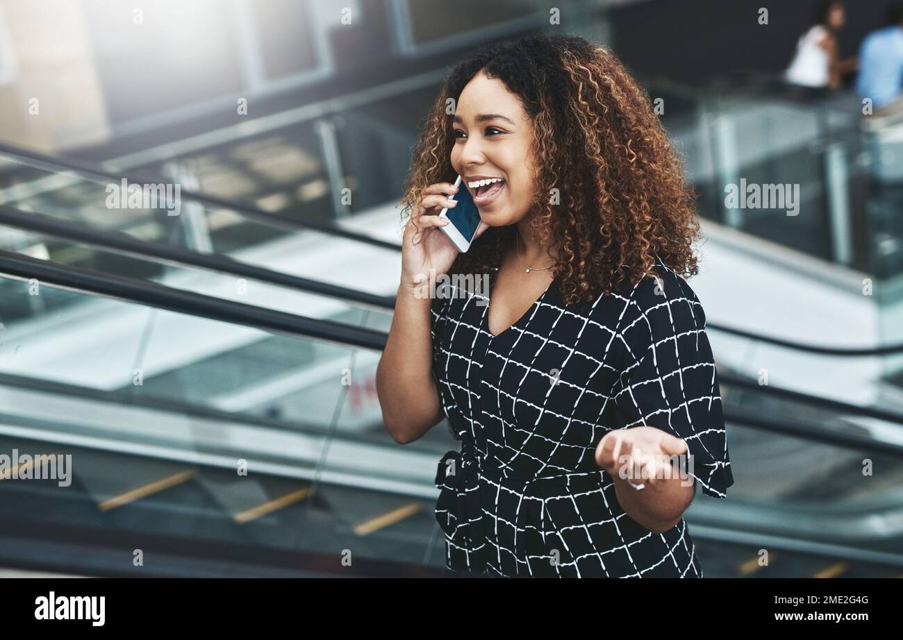 Im entusiasta di sentire così grande notizia. una giovane donna d'affari attraente che prende una telefonata mentre si sposta su una scala mobile in un posto di lavoro moderno. Foto Stock