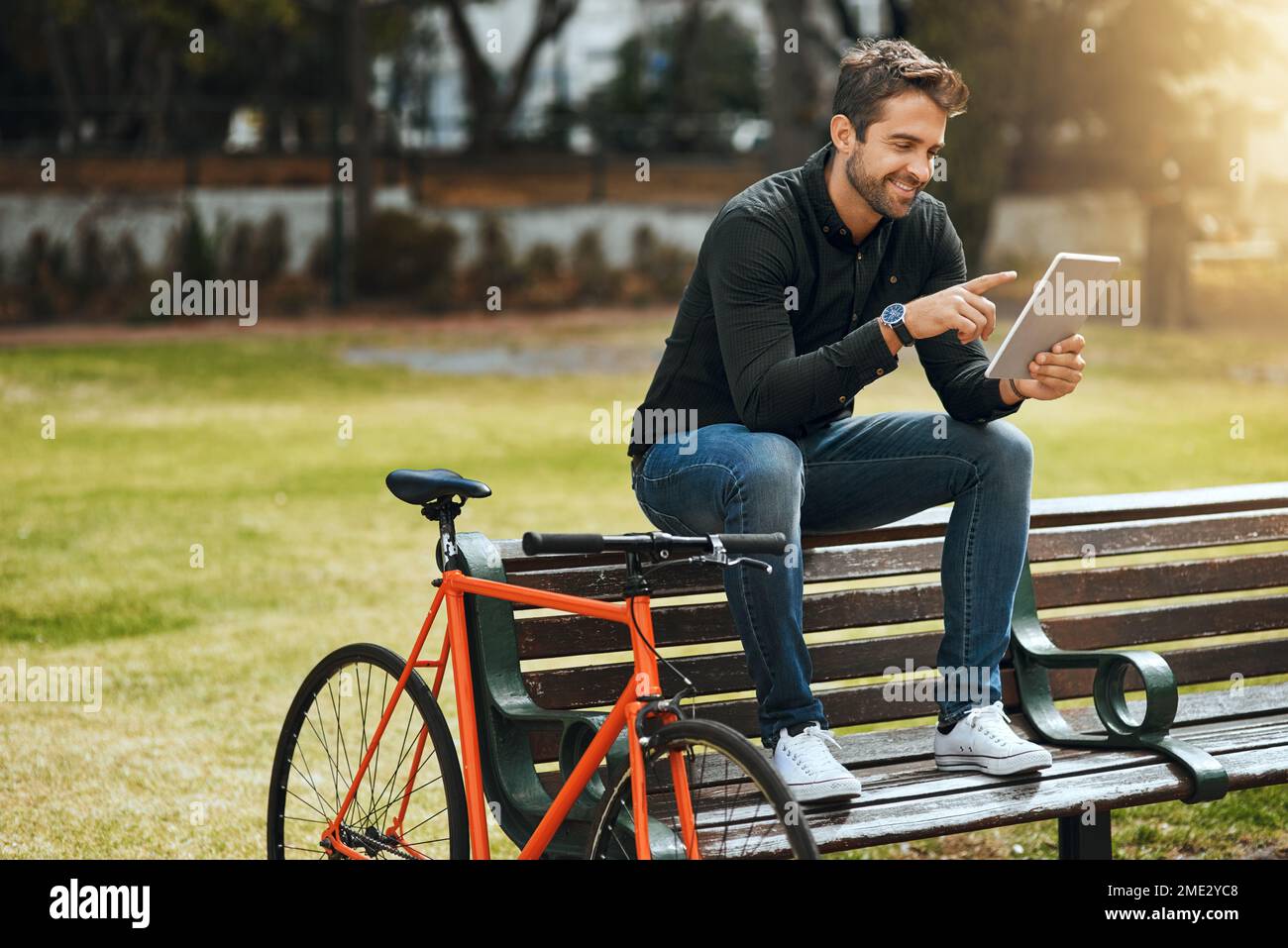 Vive la vita in modo un po' diverso. Scatto a tutta lunghezza di un bel giovane uomo che usa il suo tablet mentre si siede su una panca del parco. Foto Stock