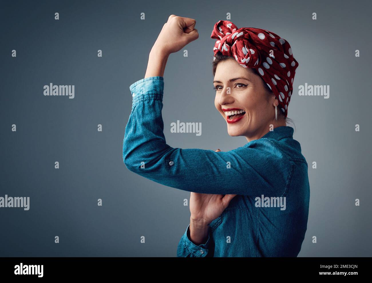 Il femminismo è il futuro. Studio shot di una giovane donna attraente flexing il suo bicep mentre si trova su uno sfondo grigio. Foto Stock