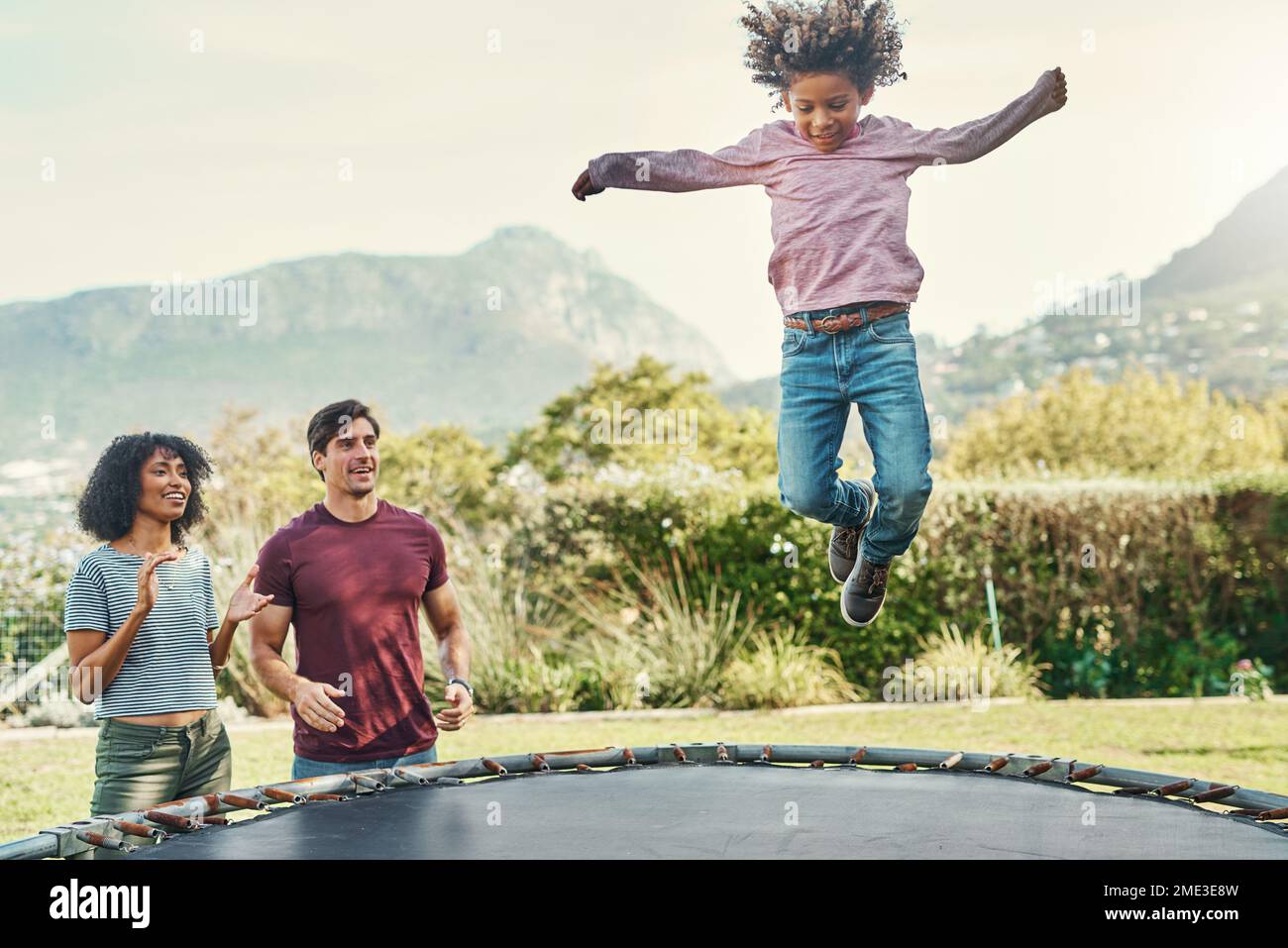 HES il nostro piccolo volantino. un adorabile ragazzino che salta su un trampolino con i suoi genitori che guardano da vicino sullo sfondo. Foto Stock
