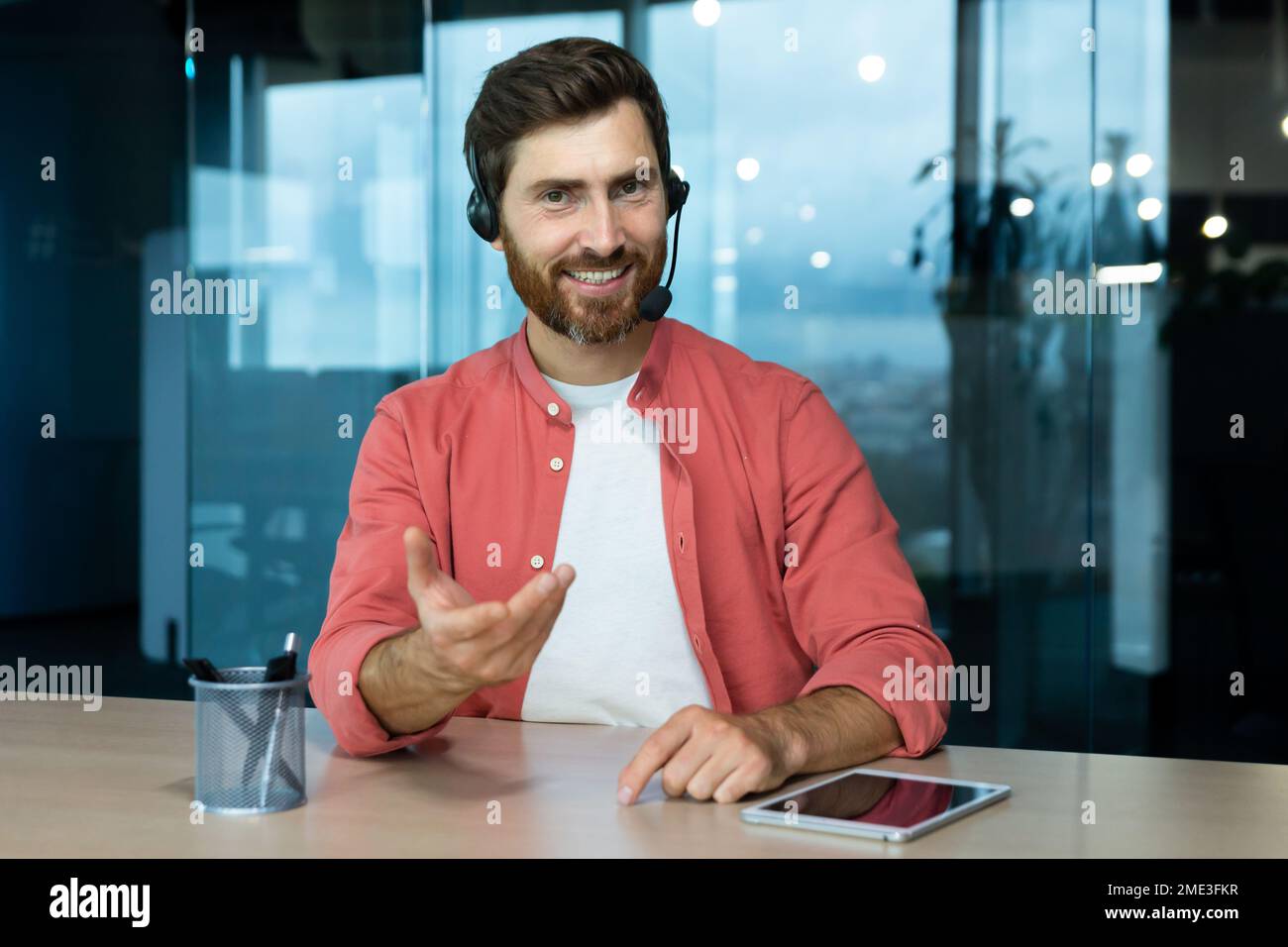 Webcam vista pov, uomo in ufficio con cuffie per videochiamate sorridente e guardando la fotocamera, venditore di affari online comunica con i clienti, lavora in remoto laptop a riunioni online colleghi Foto Stock