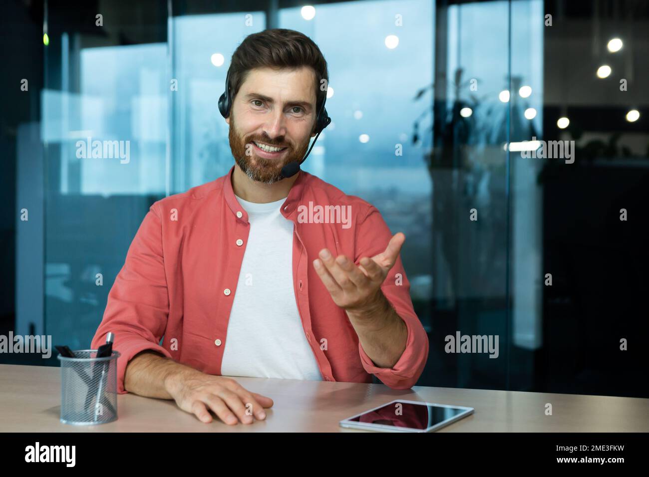 Webcam vista pov, uomo in ufficio con cuffie per videochiamate sorridente e guardando la fotocamera, venditore di affari online comunica con i clienti, lavora in remoto laptop a riunioni online colleghi Foto Stock