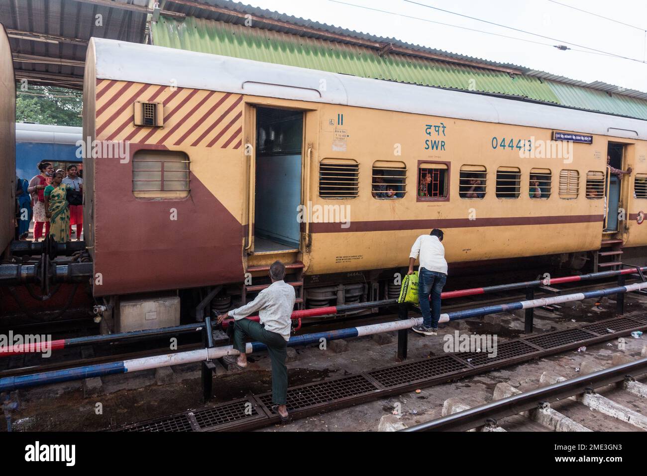 Persone che attraversano le rotaie pericolosamente per entrare in treno alla stazione di Bengaluru cantonment Foto Stock