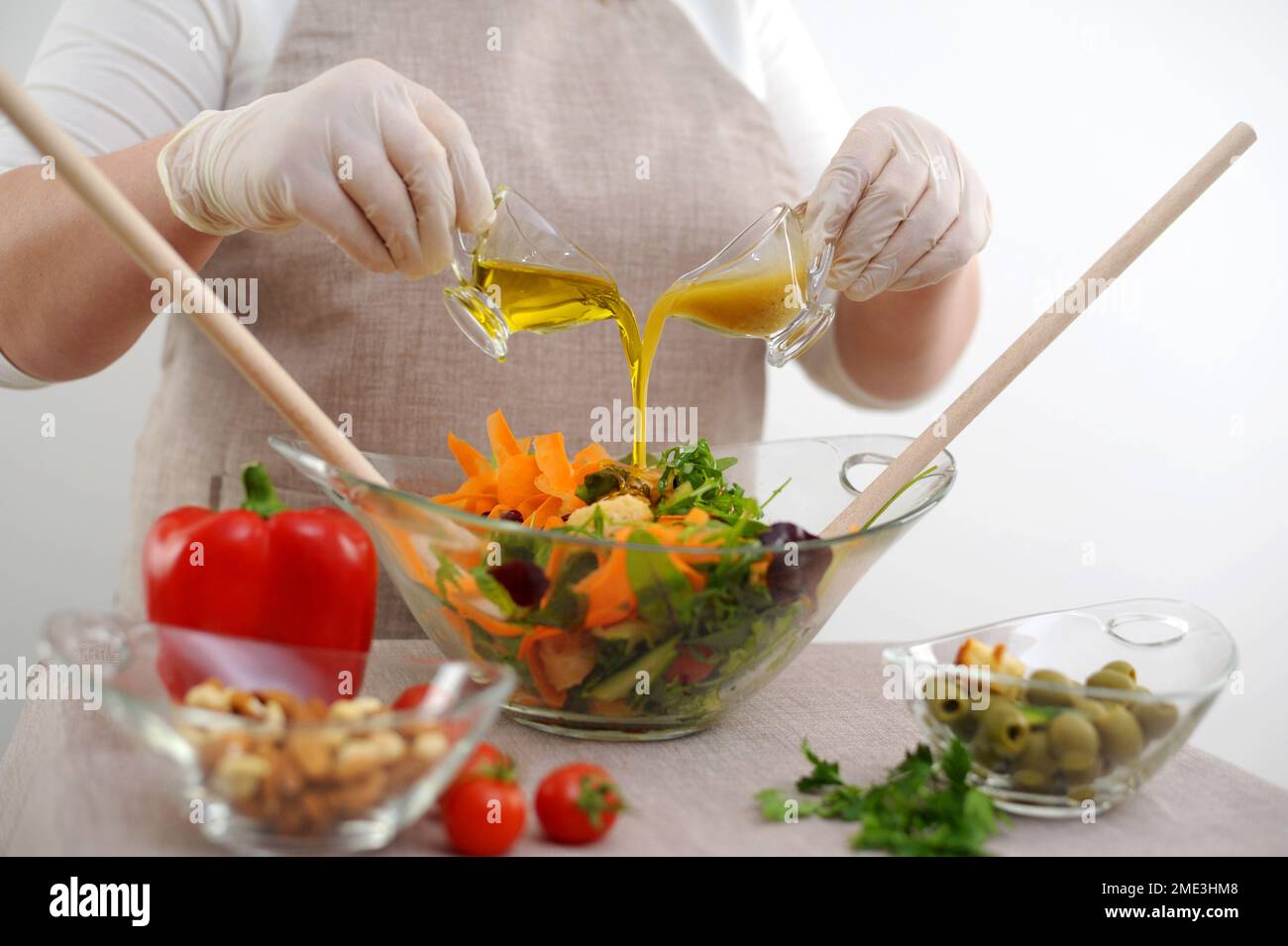 cuoci in guanti sterili prepara deliziosi cibi sani versare condimento in insalata in un recipiente di vetro da due brocche di insalata di olio d'oliva e salsa con senape e ingredienti di miele Foto Stock