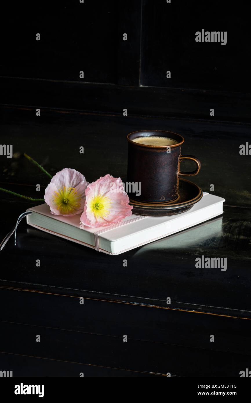 Islanda fiori di papavero in tazza di caffè su diario su pianoforte nero Foto Stock