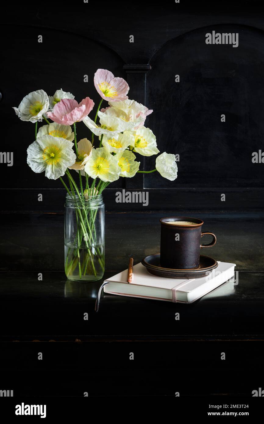 Fiori freschi di papavero islandese in vaso di vetro da una tazza di caffè e diario su pianoforte nero Foto Stock