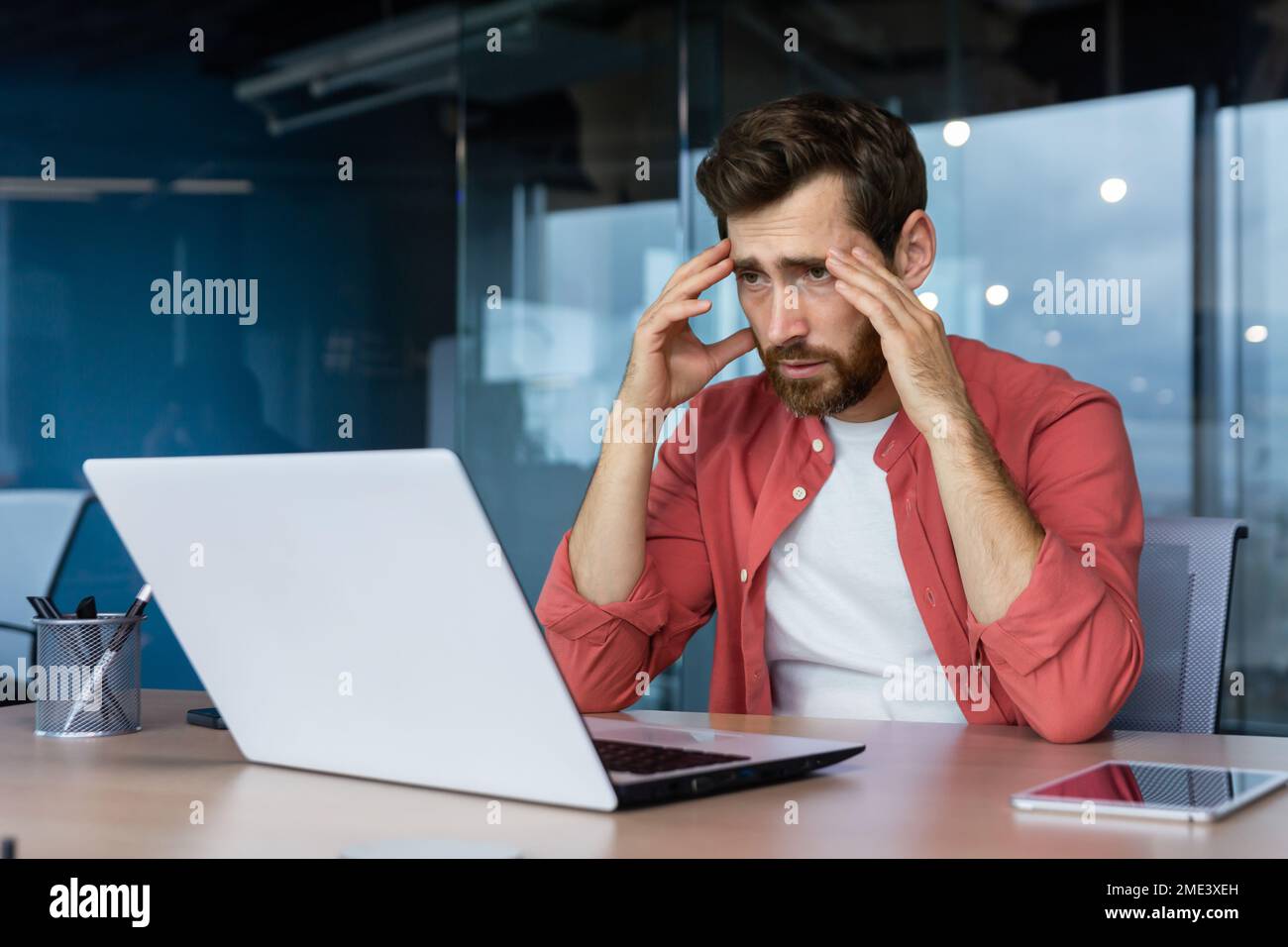 Un uomo d'affari frustrato depresso sul posto di lavoro che lavora su un notebook, un uomo in camicia turbato e triste dispiaciuto con risultati di lavoro e risultati negativi all'interno dell'ufficio. Foto Stock