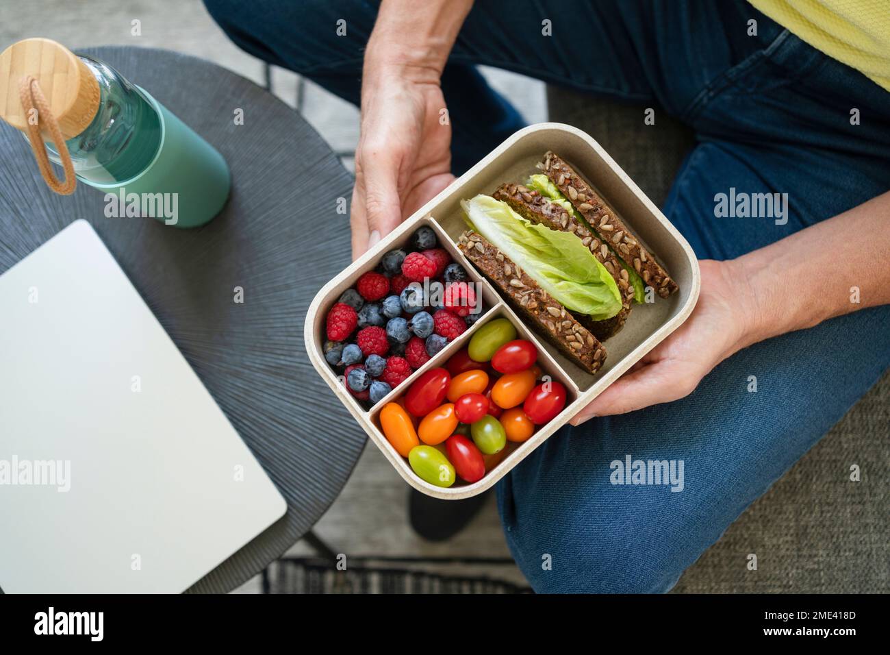 Mani di un uomo che tiene il pranzo al sacco con cibo sano sul divano Foto Stock