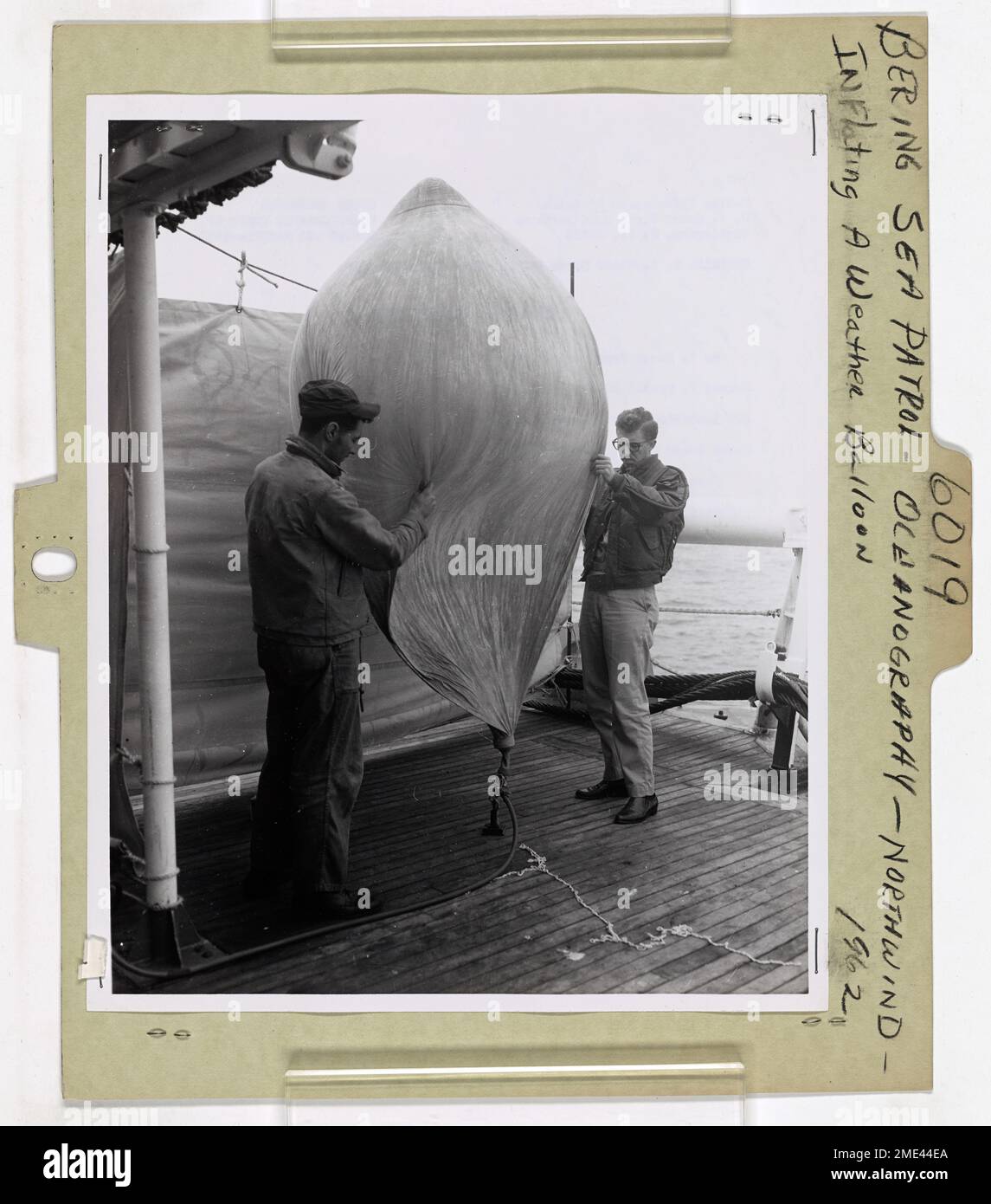 Gonfiaggio di una mongolfiera. STATI UNITI Il compagno dell'aerografo della Guardia costiera Frank A. Perdue aiuta l'osservatore Norman E. Caroll degli Stati Uniti Weather Bureau per gonfiare una mongolfiera per il lancio nell'atmosfera superiore dal ponte di volo degli Stati Uniti Guardia costiera rompighiaccio Northwind. I dati sulla pressione dell'aria superiore, l'umidità e la velocità dei venti, sono stati raccolti mediante l'uso di palloncini meteorologici in aggiunta alla cartografia e alla verifica delle profondità dell'acqua effettuate durante il sondaggio oceanografico del Northwind sul Mare di Bering settentrionale e sulle acque internazionali al largo della Siberia tra luglio e ottobre. Partecipazione a questo pr Foto Stock