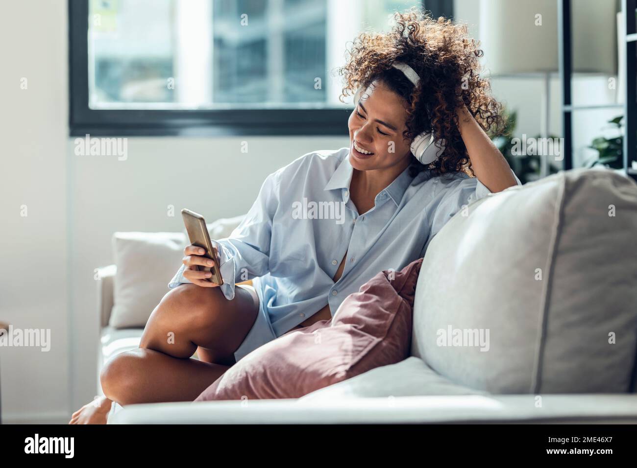 Donna felice che usa il telefono cellulare seduto sul divano in soggiorno Foto Stock