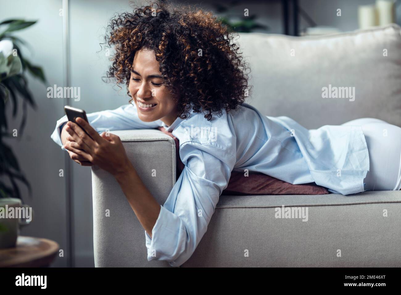 Buona donna messaggi di testo su smartphone sdraiato sul divano Foto Stock