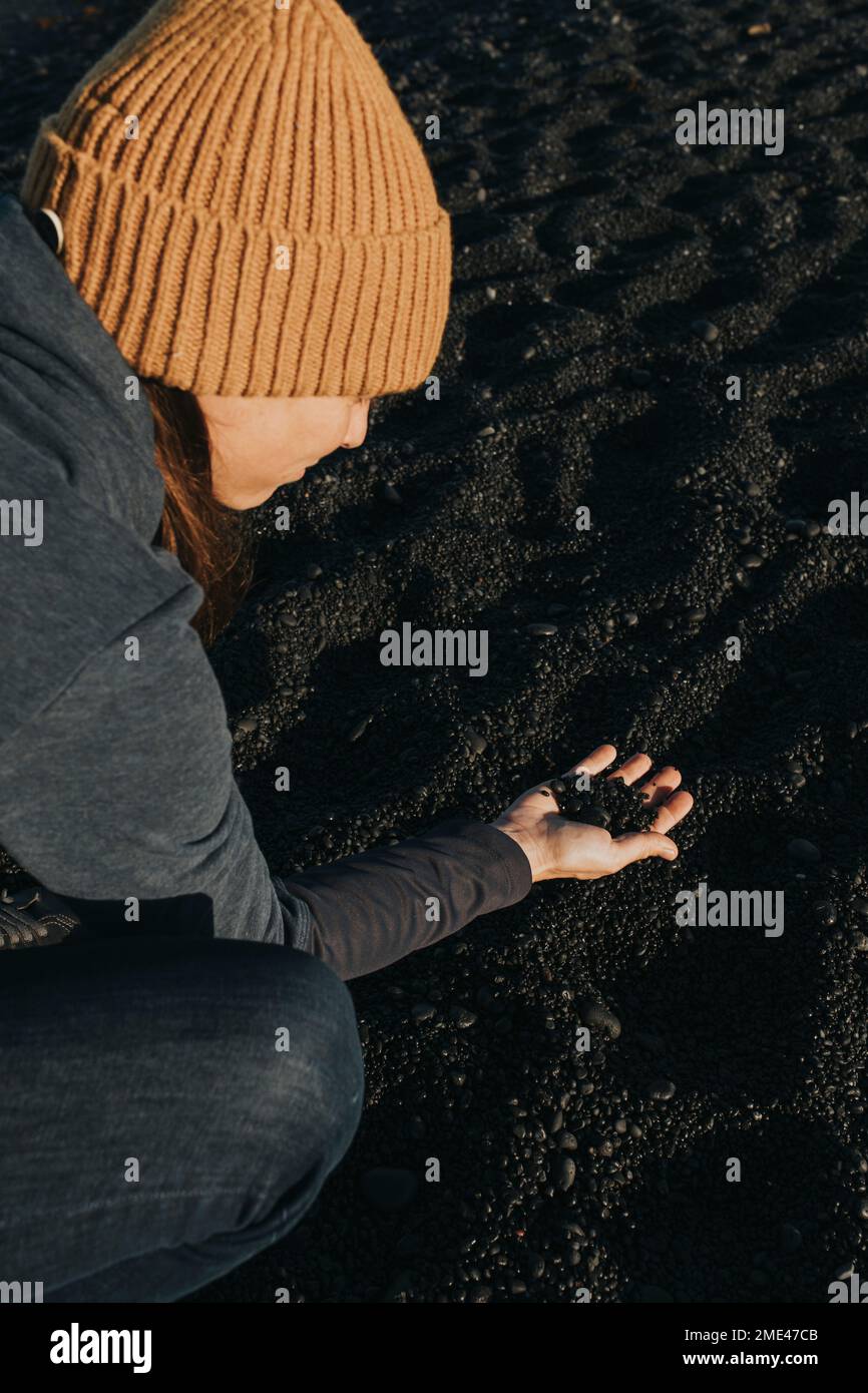 Donna che raccoglie sabbia nera sulla spiaggia vulcanica Foto Stock