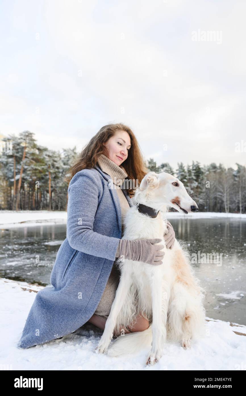 Donna che accarezzava il cane levriero davanti al lago ghiacciato Foto Stock