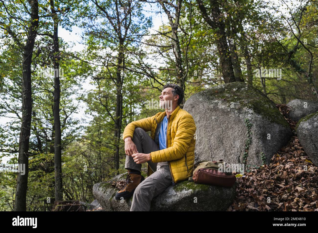 Uomo contemplativo con zaino seduto sulla roccia nella foresta Foto Stock