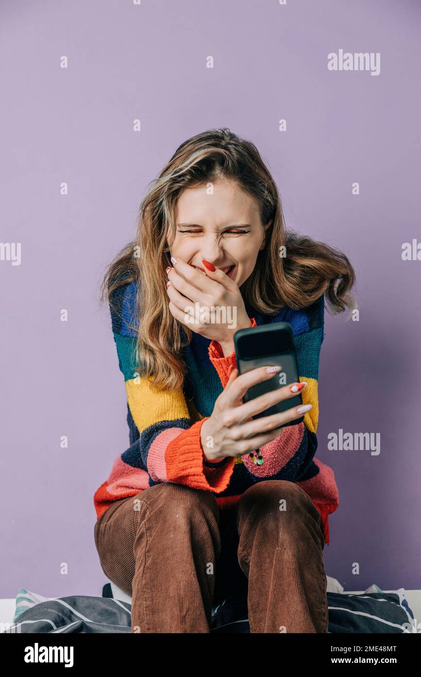 Ragazza sorridente con uno smartphone seduto su sfondo viola Foto Stock