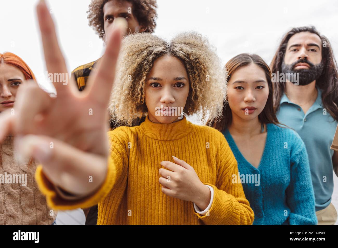 Donna che mostra un segno di pace con diversi manifestanti Foto Stock