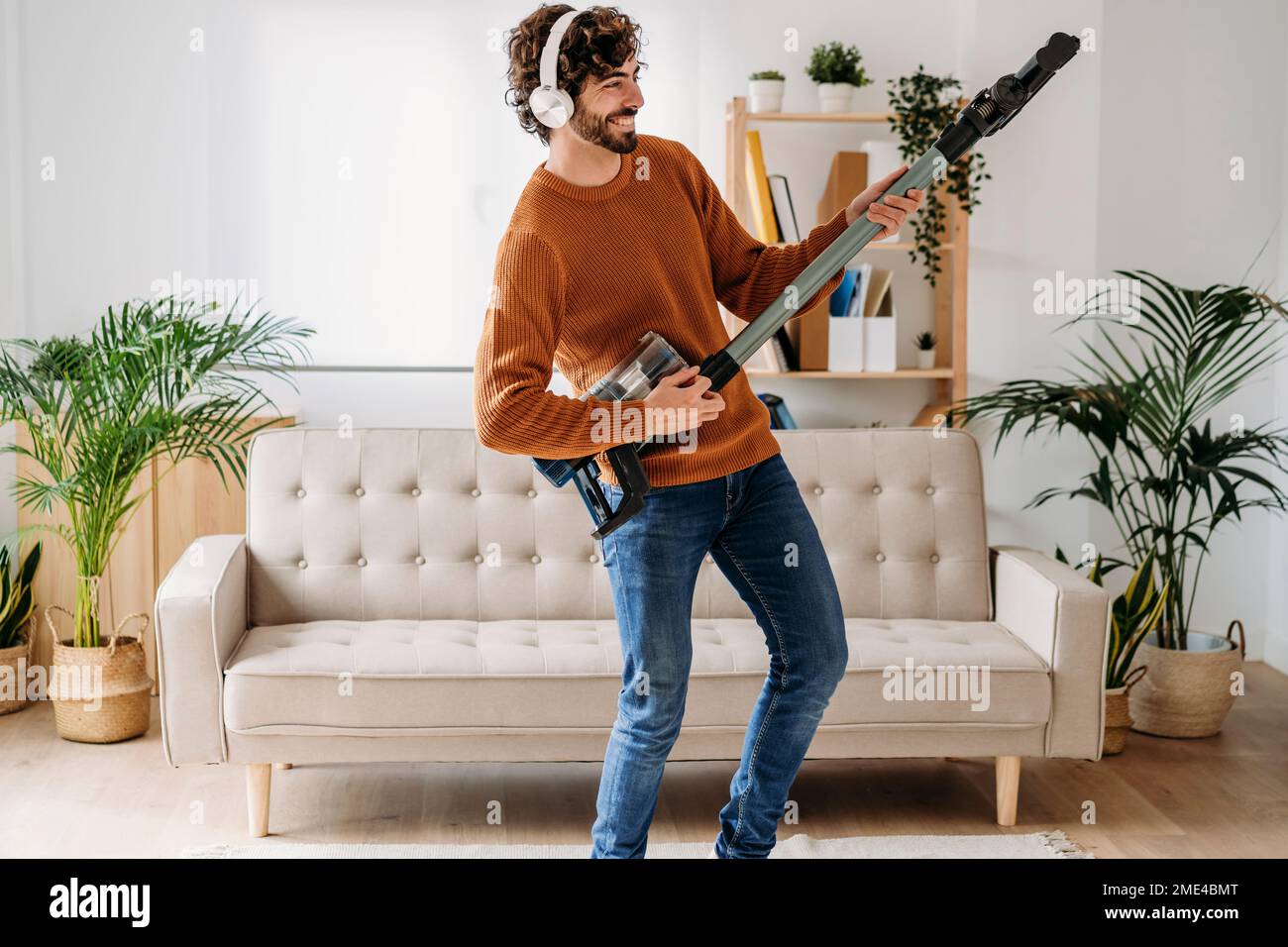 Felice giovane uomo che balla e suona la chitarra con l'aspirapolvere a casa Foto Stock