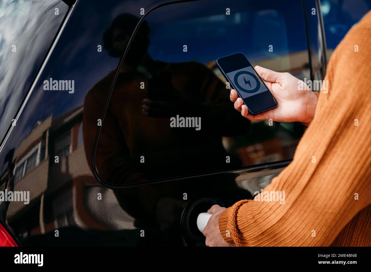 Uomo che utilizza lo smartphone e ricarica l'auto presso la stazione di ricarica per veicoli elettrici Foto Stock