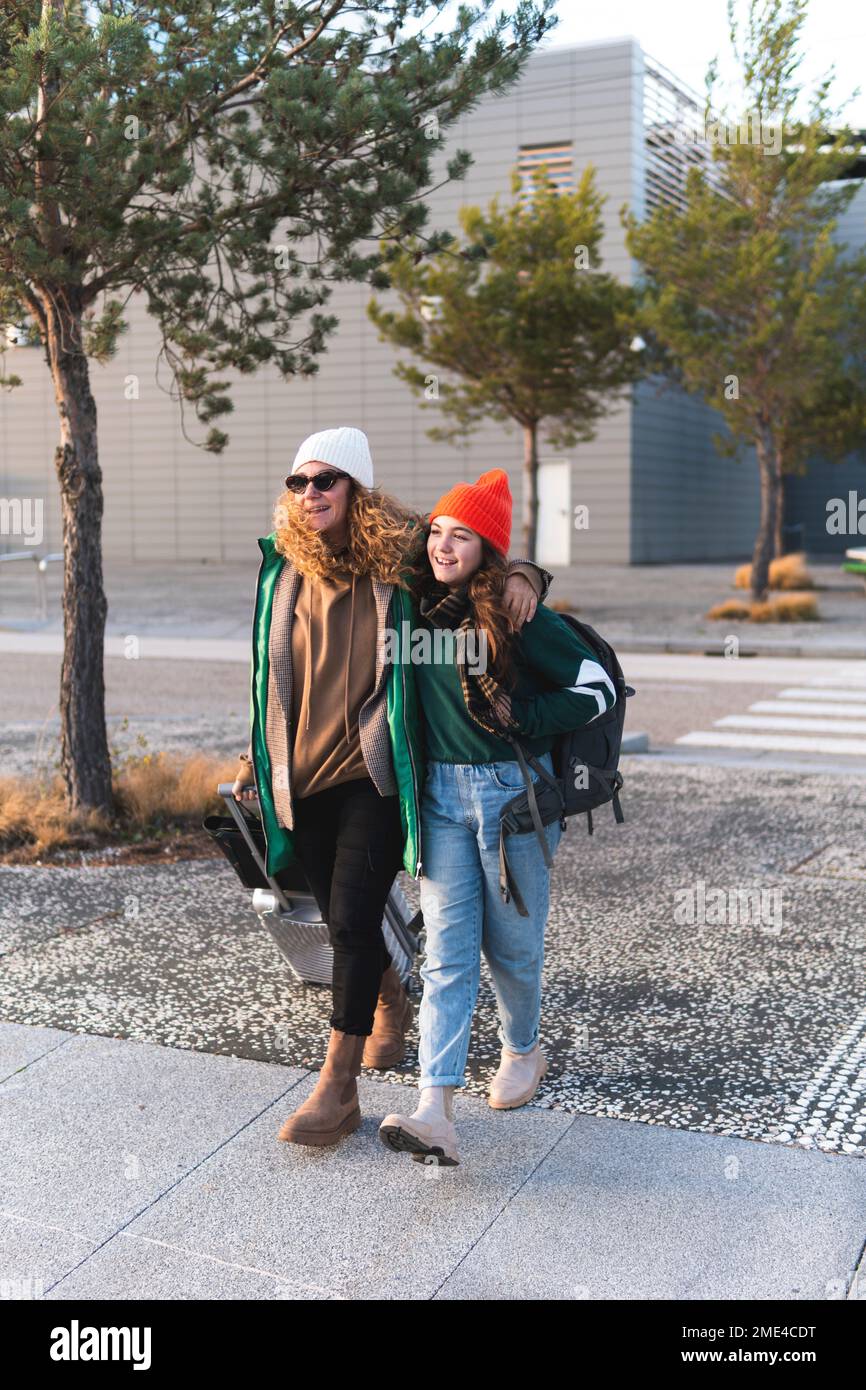 Madre e figlia che attraversano la strada tirando valigia Foto Stock