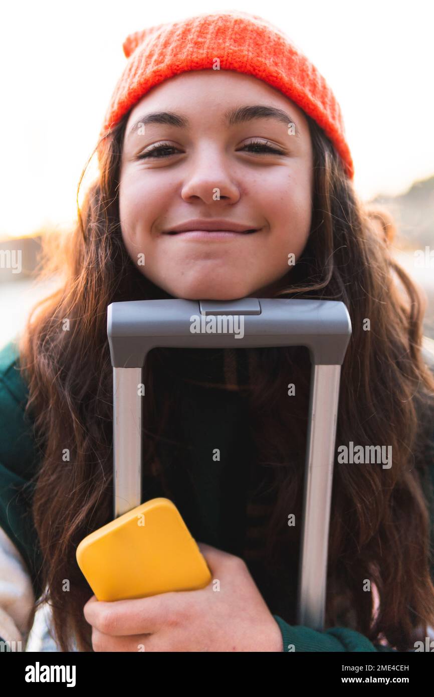Ragazza sorridente che appoggia il viso sull'impugnatura della valigia Foto Stock