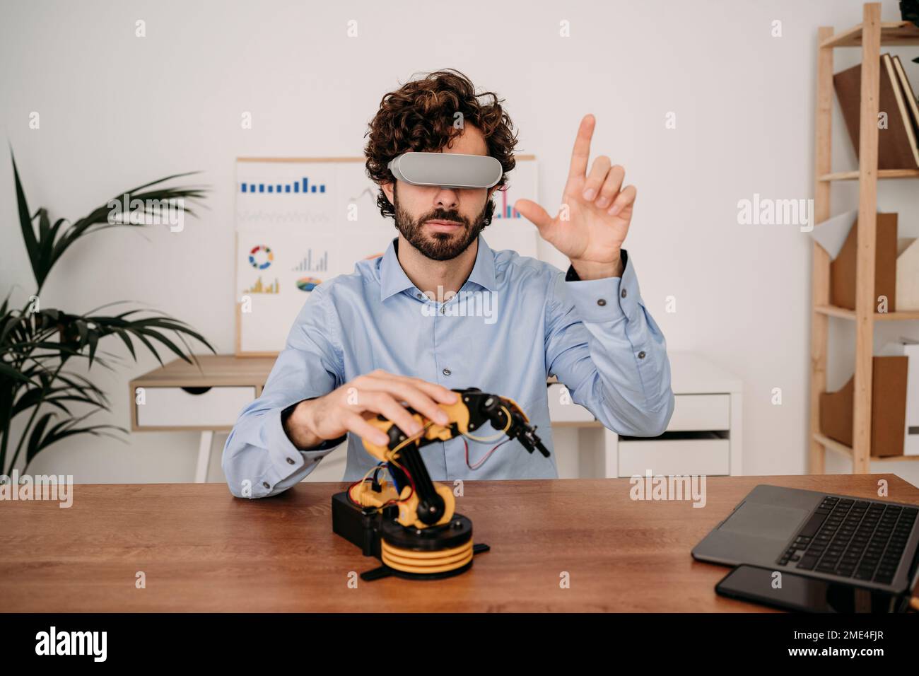 Uomo d'affari che indossa occhiali per realtà virtuale con braccio robotico sulla scrivania in ufficio Foto Stock