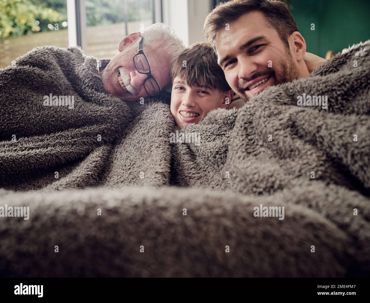 Buon nonno, padre e figlio che si snuggling sotto una coperta sul divano in soggiorno Foto Stock
