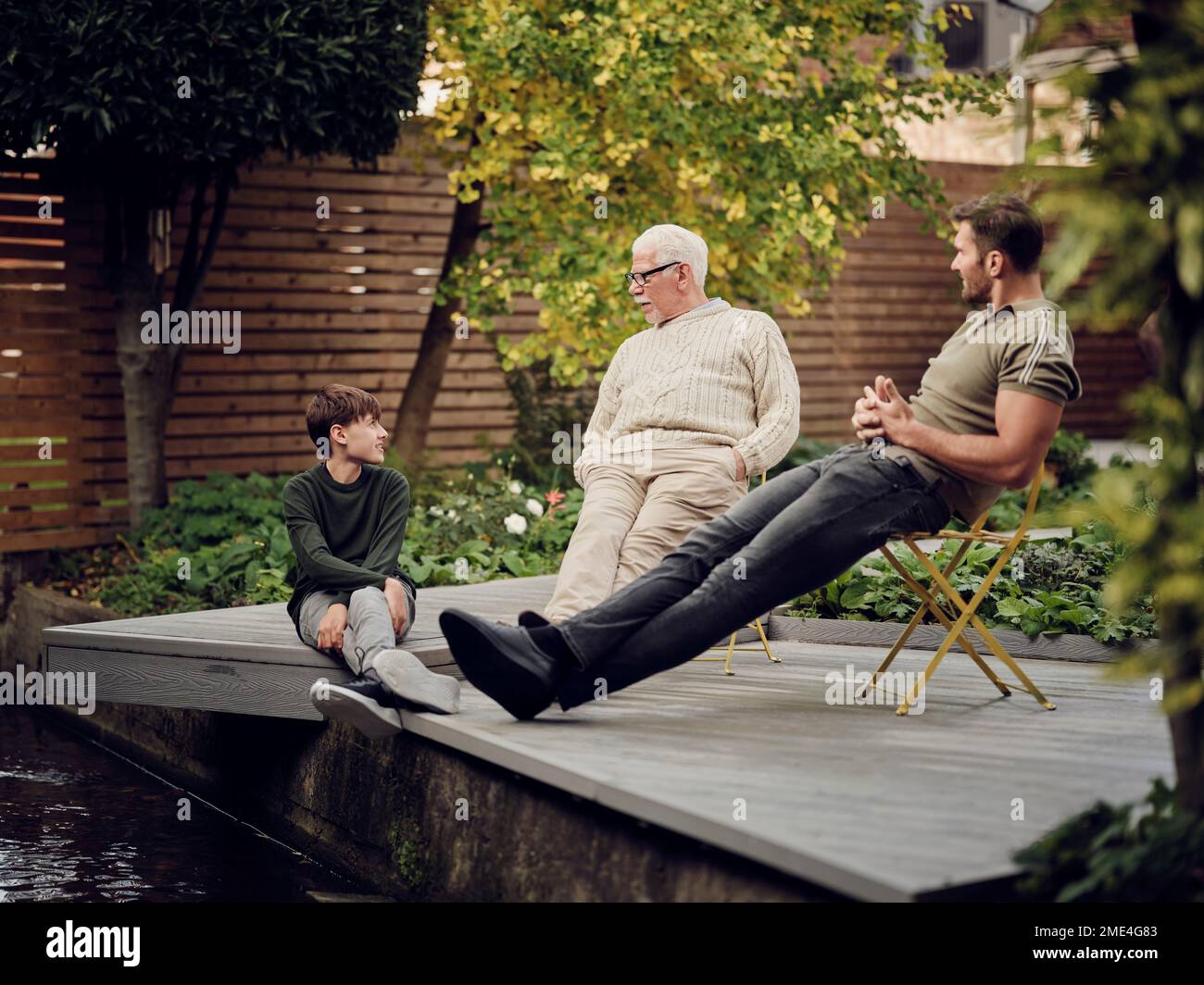 Padre, figlio e nipote seduti al laghetto del giardino che parlano e si rilassano Foto Stock