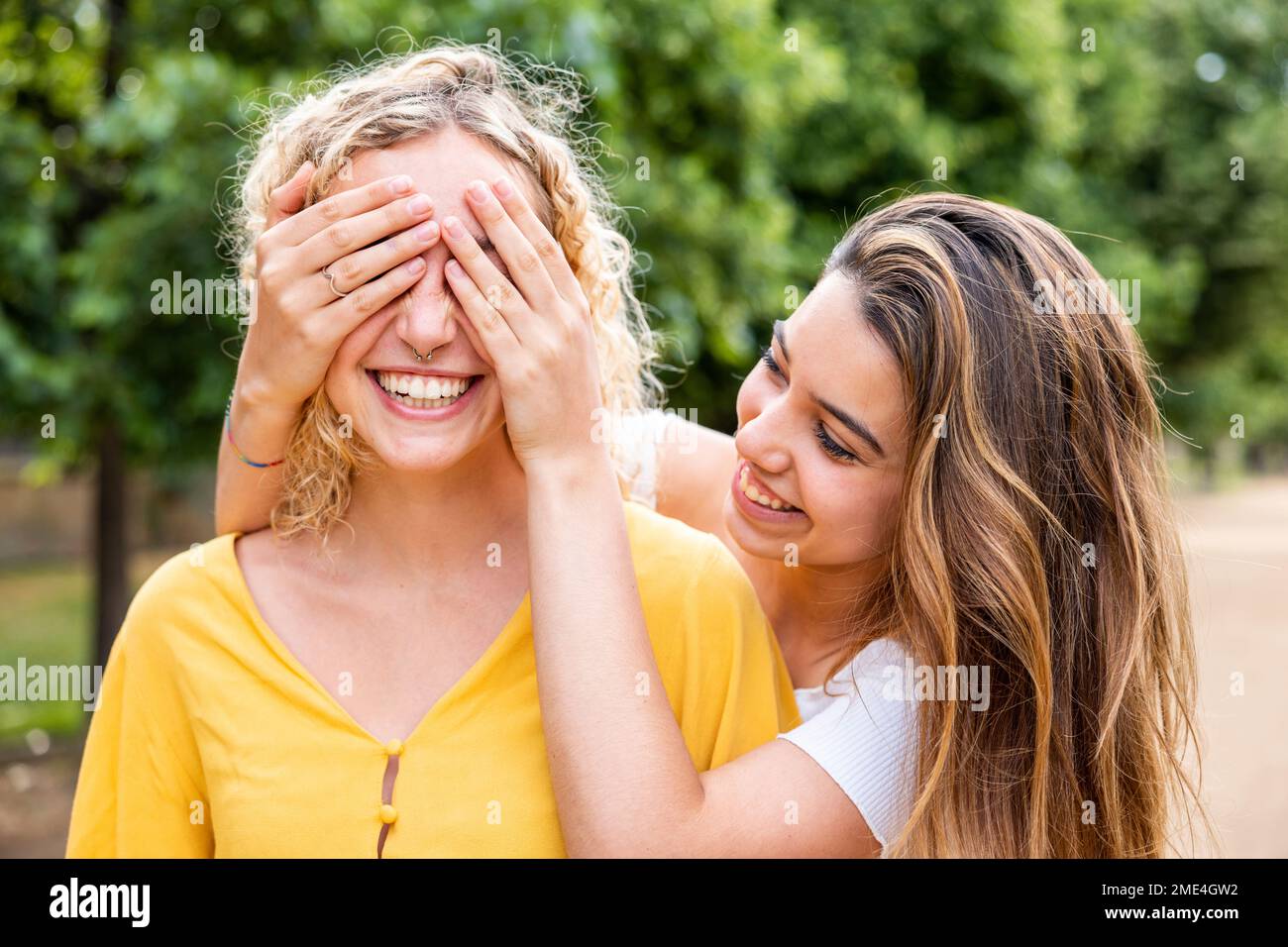 Donna sorridente che copre gli occhi dell'amico con le mani nel parco Foto Stock
