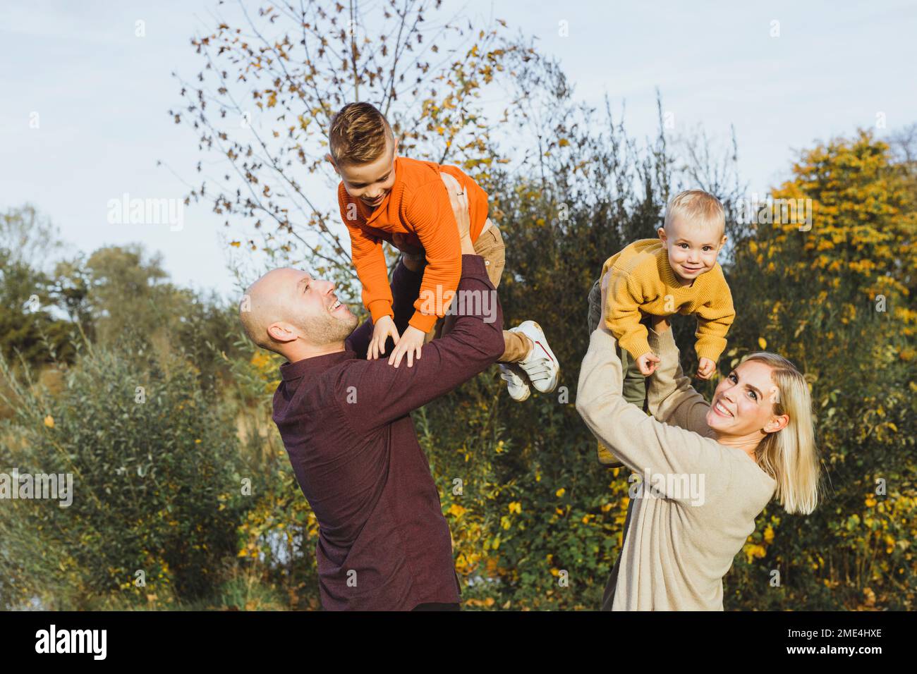 Genitori giocosi che sollevano i bambini in autunno Foto Stock