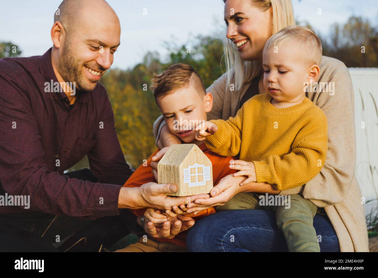 Genitori felici con i bambini che tengono la casa del modello nella natura Foto Stock