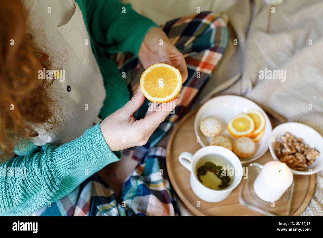 Donna che tiene la fetta di arancia seduta sul letto a casa Foto Stock