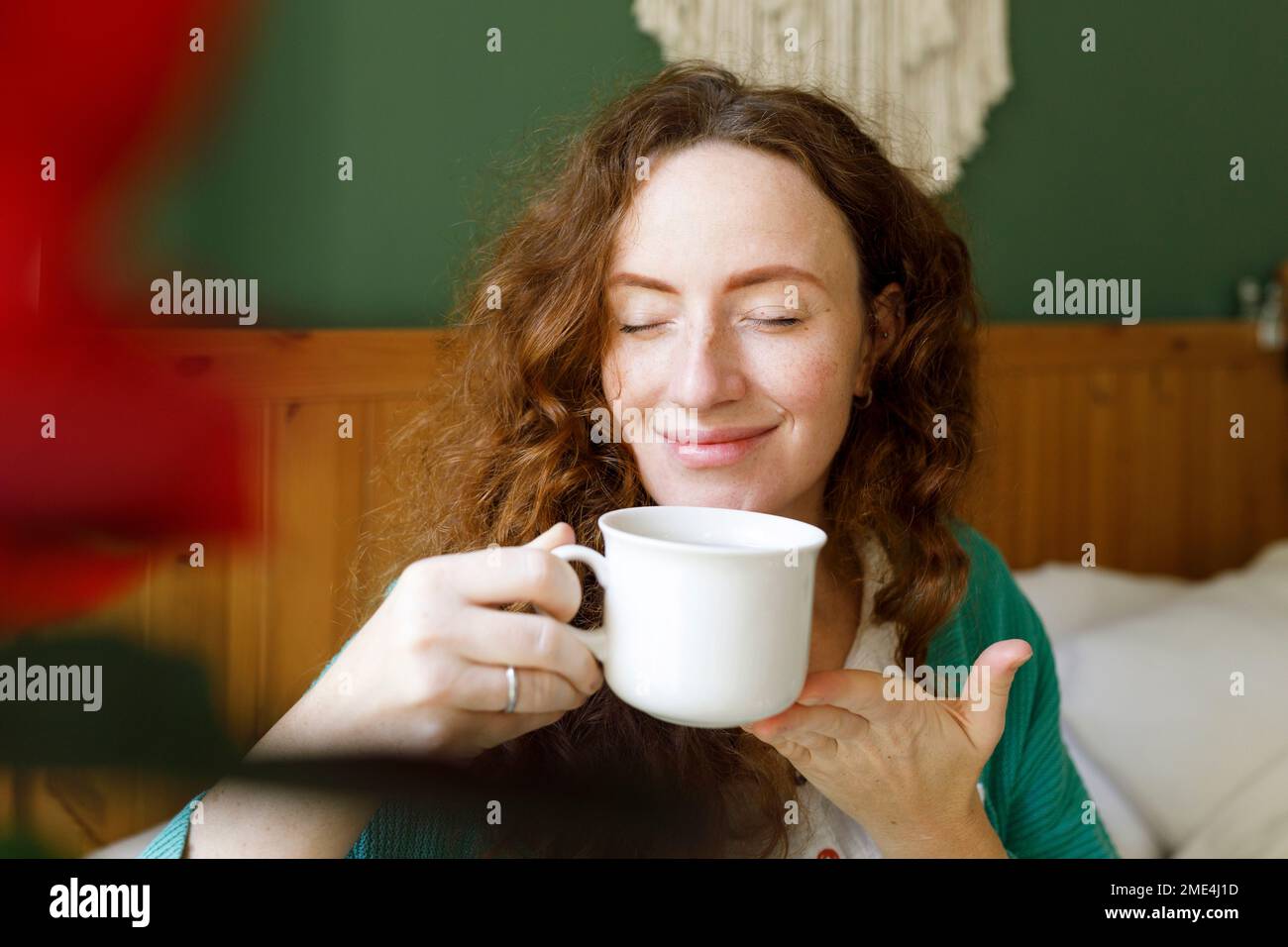 Donna sorridente con gli occhi chiusi avendo il tè a casa Foto Stock