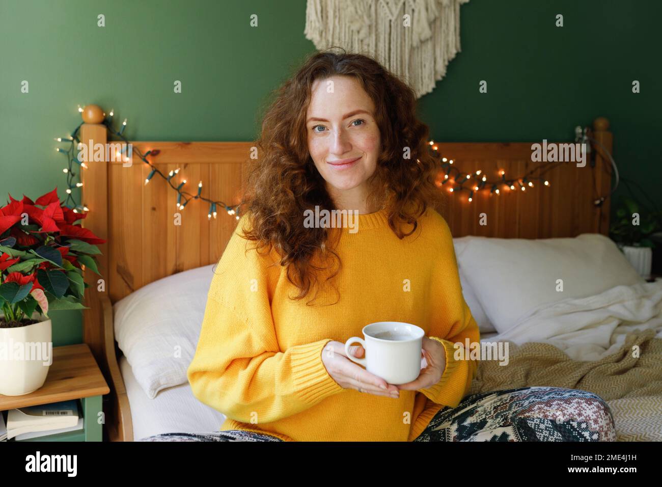 Donna sorridente che tiene una tazza di tè a letto a casa Foto Stock