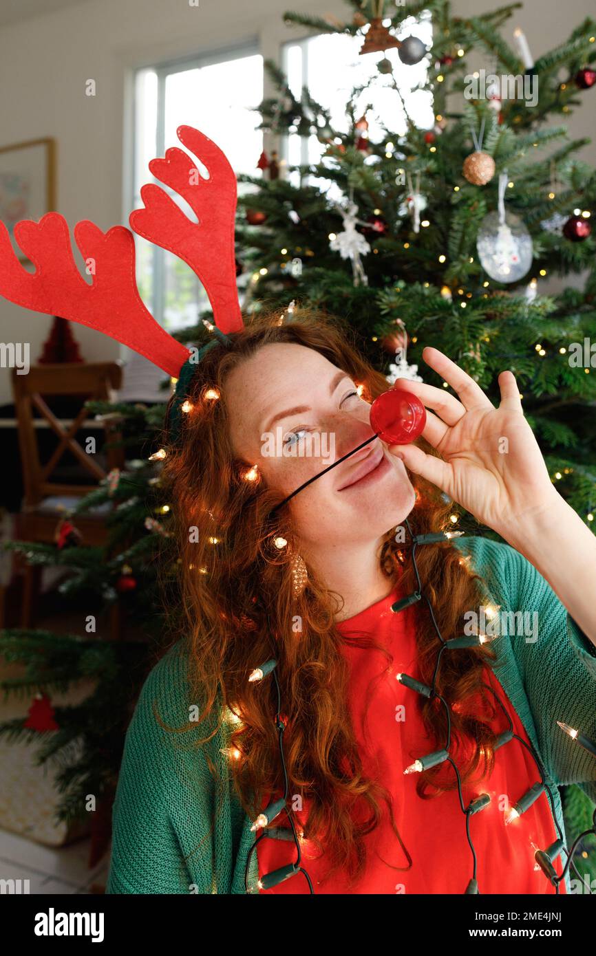 Donna sorridente che indossa il naso dei clown con le luci di Natale a casa Foto Stock