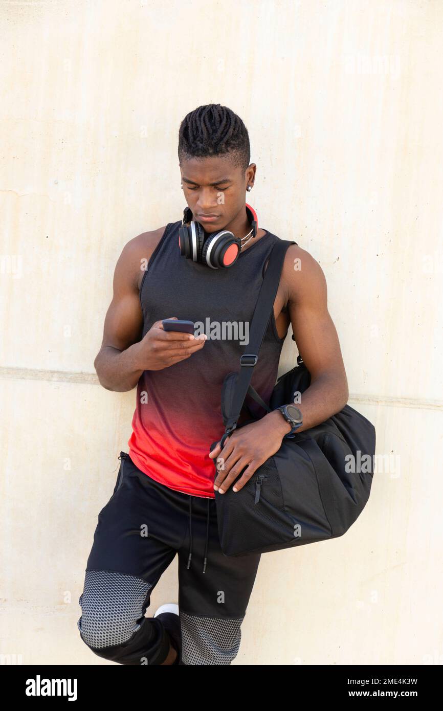 Un giovane uomo che tiene la borsa da palestra con uno smartphone appoggiato alla parete Foto Stock