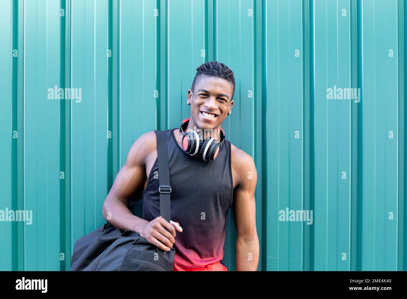 Felice giovane uomo con la borsa palestra appoggiata sulla parete verde corrugata Foto Stock