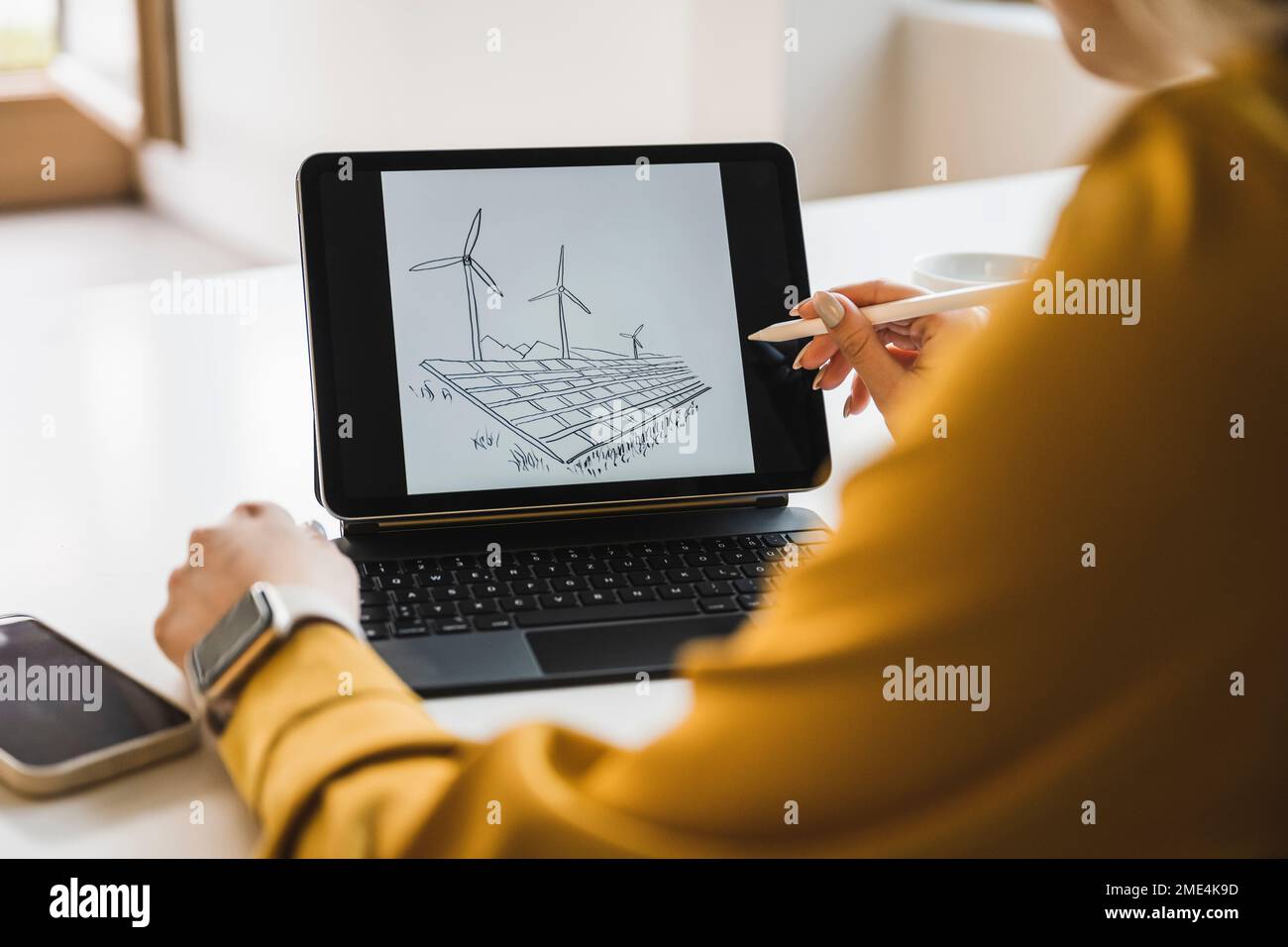 Donna d'affari che disegna turbine eoliche e pannelli solari su tablet PC con penna digitalizzata Foto Stock