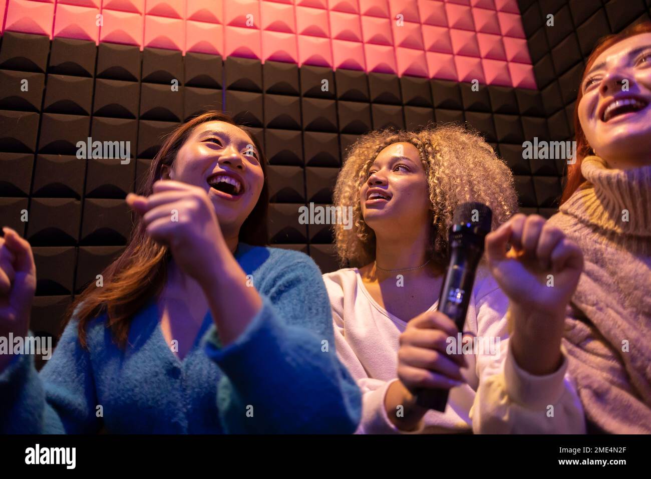 Amici felici che si divertono a tenere il microfono nella sala giochi Foto Stock