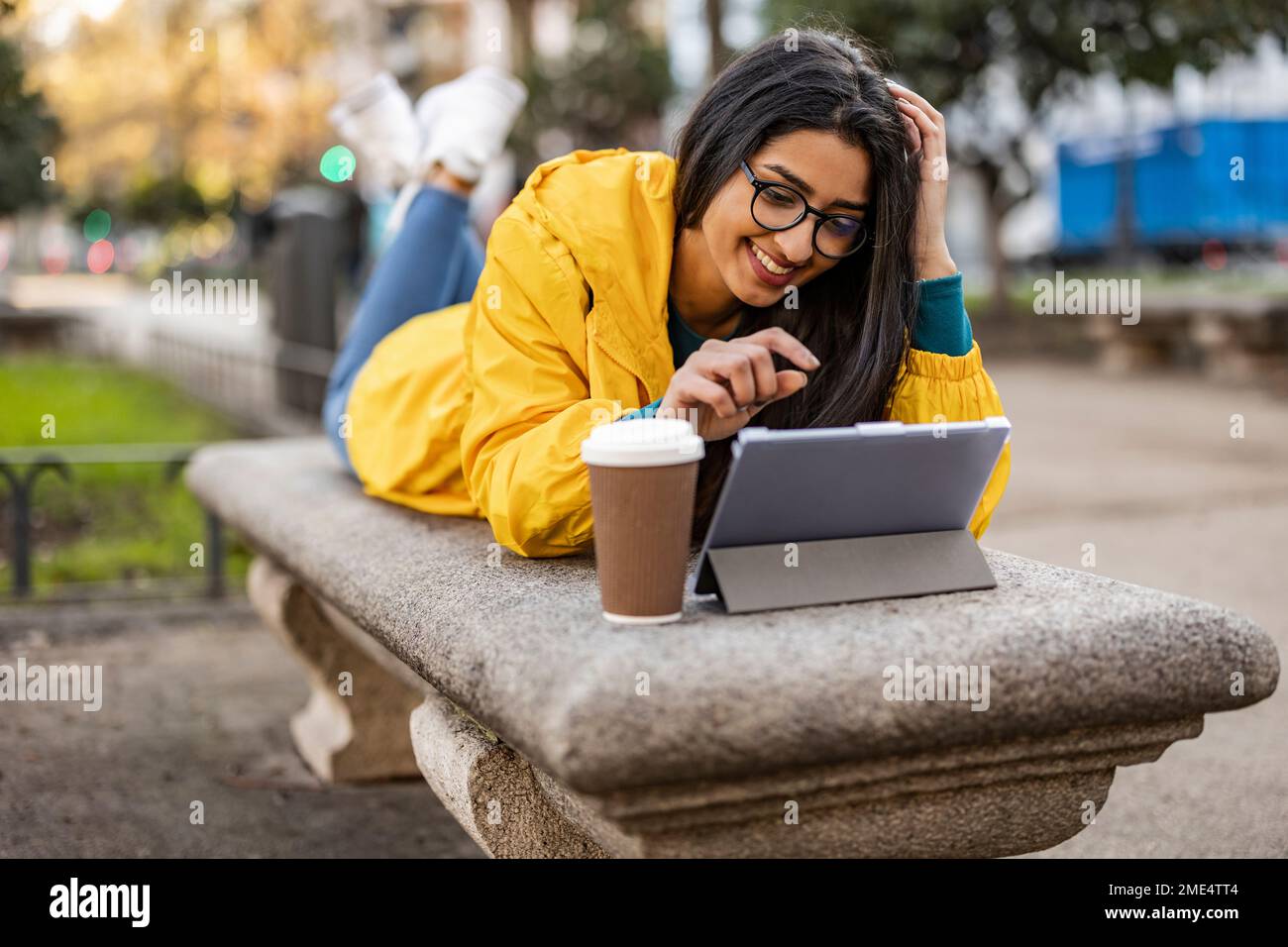 Felice giovane donna che usa un tablet PC sdraiato sul banco Foto Stock