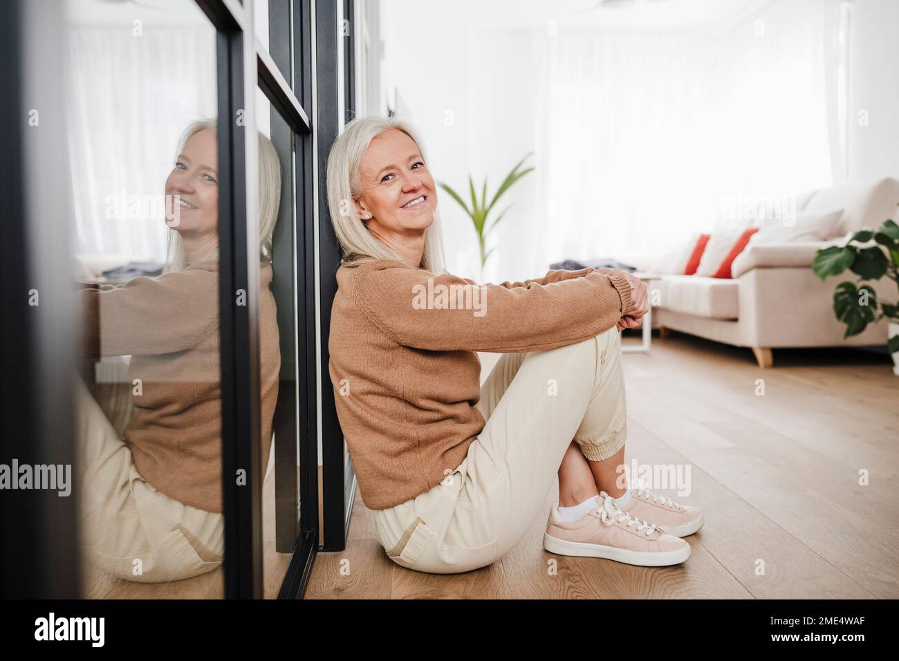 Donna felice seduta sul pavimento in soggiorno Foto Stock