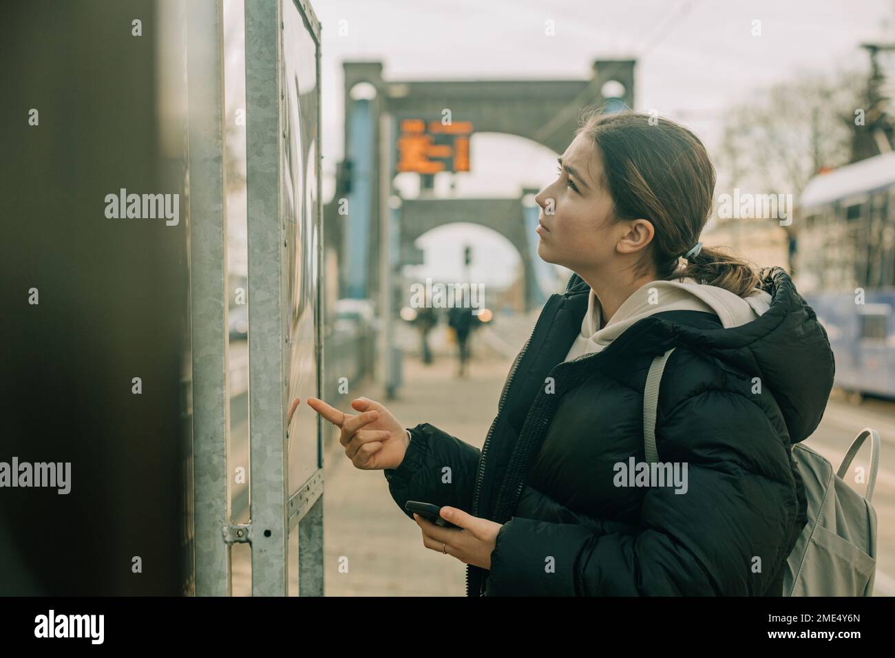 Ragazza adolescente che controlla arrivo partenza bordo alla stazione del tram Foto Stock