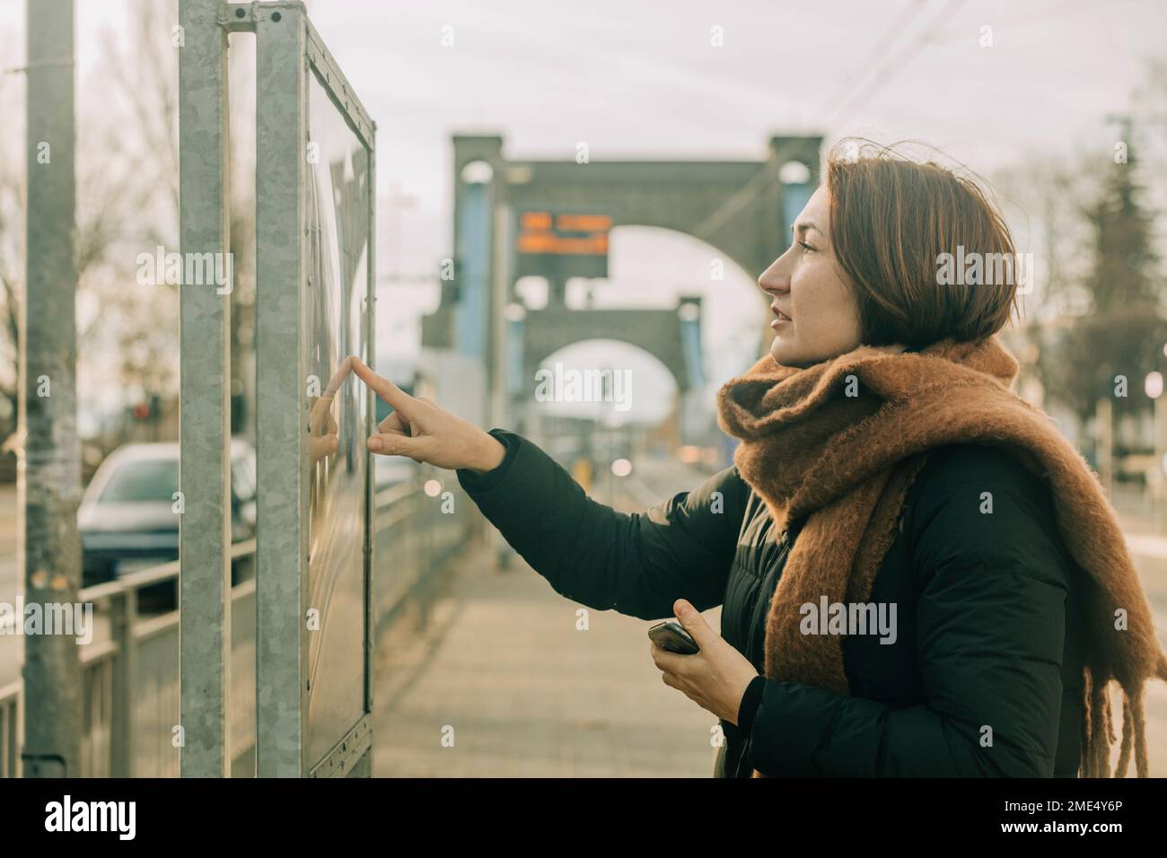 Donna matura che controlla arrivo partenza bordo alla stazione del tram Foto Stock