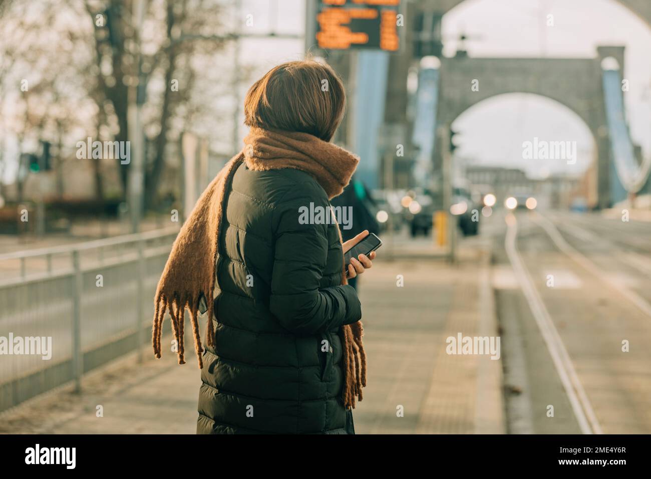 Donna matura in piedi con smartphone alla stazione del tram Foto Stock