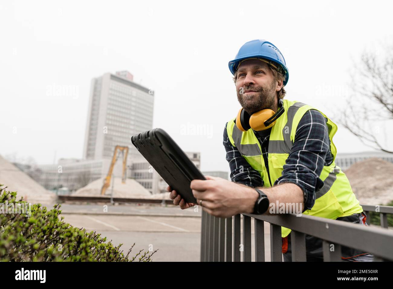 Un lavoratore maturo sorridente con un tablet PC appoggiato sulla ringhiera Foto Stock