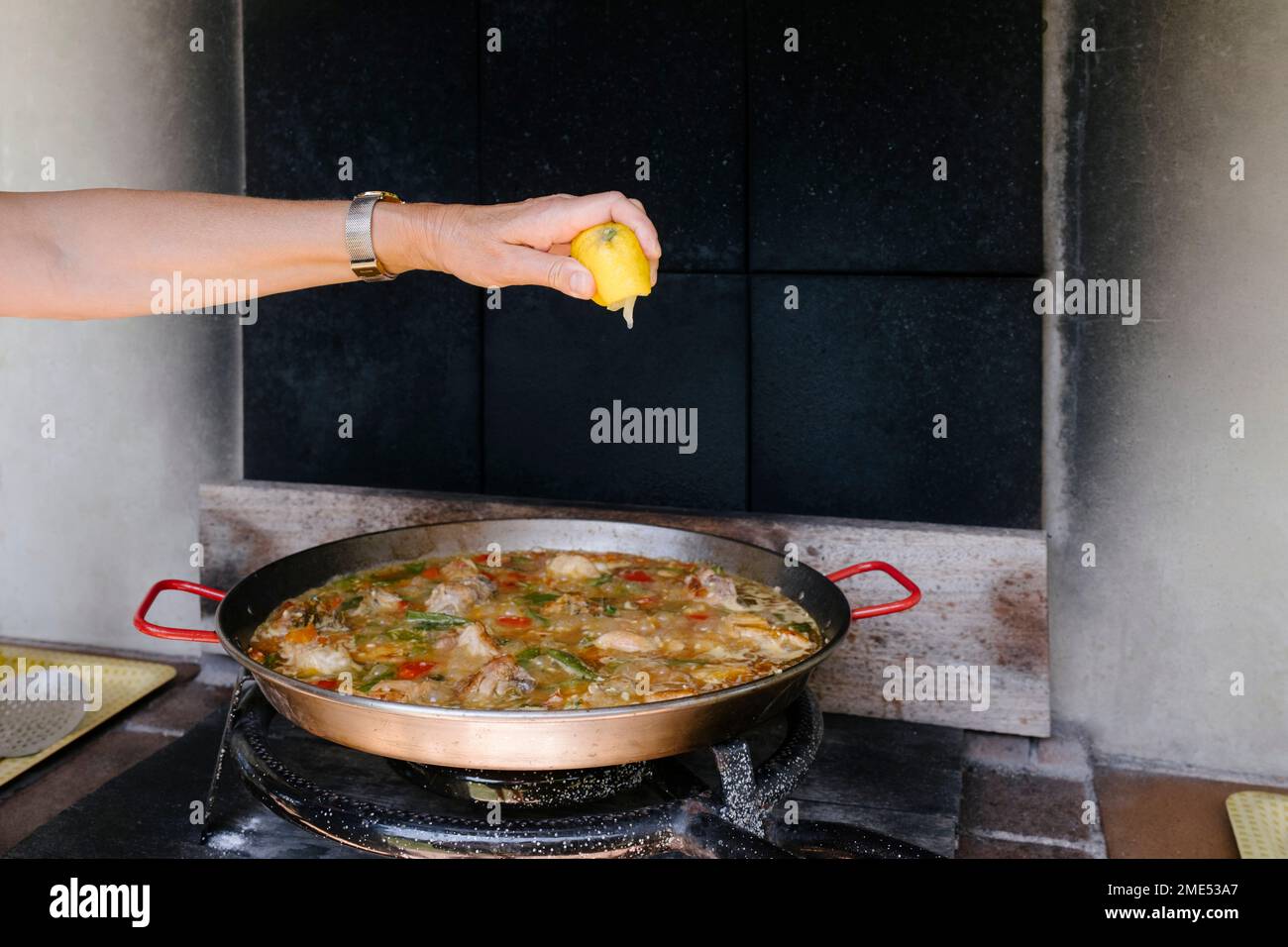 Donna spremitura limone su paella in cucina all'aperto Foto Stock